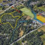 Aerial map showing a central park with white-dashed boundary, yellow looped Park Trails, blue streams, and surrounding streets including Telegraph Rd and E. Bakerview Dr; orange AF Housing area nearby.