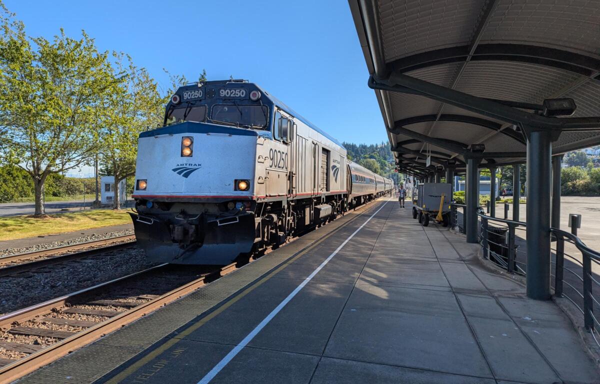 Blue Amtrak locomotive at a sunny station platform, number 90250 visible on the front and sides of the train, awaiting passengers.