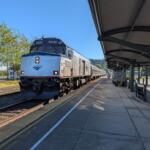 Blue Amtrak locomotive at a sunny station platform, number 90250 visible on the front and sides of the train, awaiting passengers.
