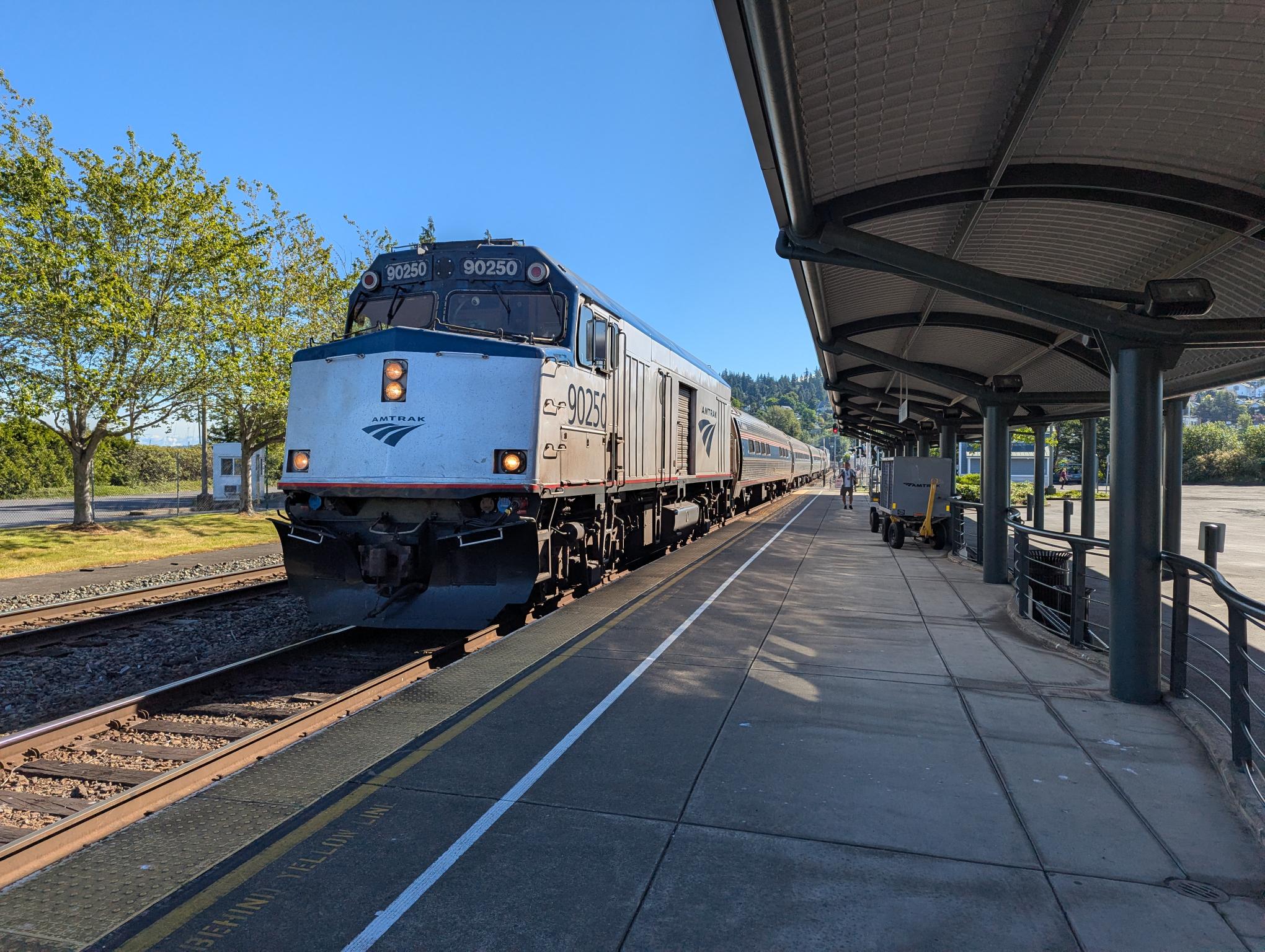 Blue Amtrak locomotive at a sunny station platform, number 90250 visible on the front and sides of the train, awaiting passengers.