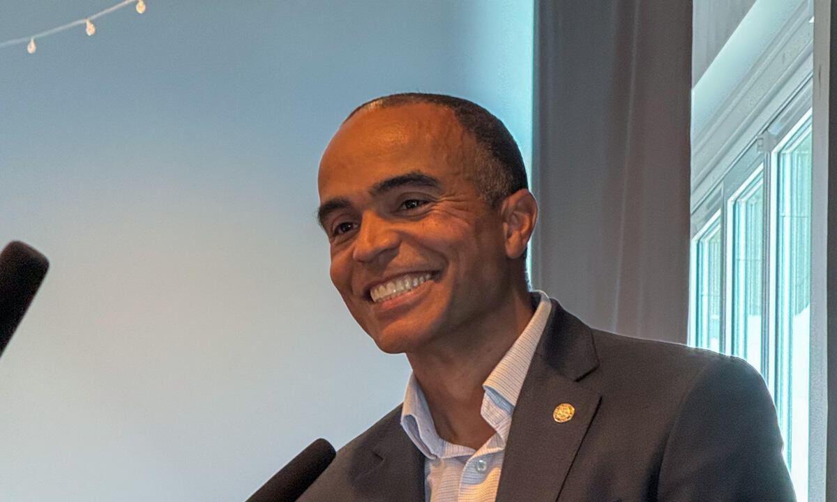 Smiling man in a dark suit speaks at a podium with two microphones in front of him.