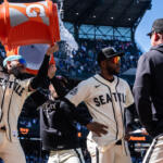 Seattle players celebrate on the field as orange Gatorade bucket dumps water over a teammate's head during a game.