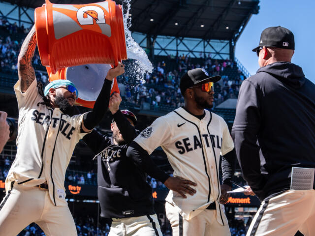 Seattle players celebrate on the field as orange Gatorade bucket dumps water over a teammate's head during a game.