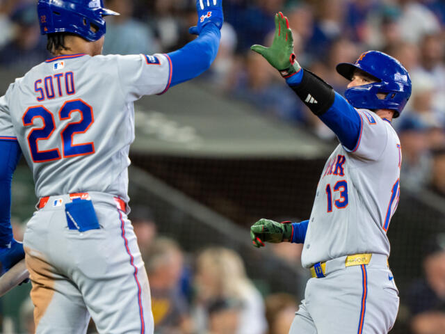 Two Mets players share a high-five on the field, Soto wearing #22 and a teammate #13 nearby against a blurred crowd backdrop.