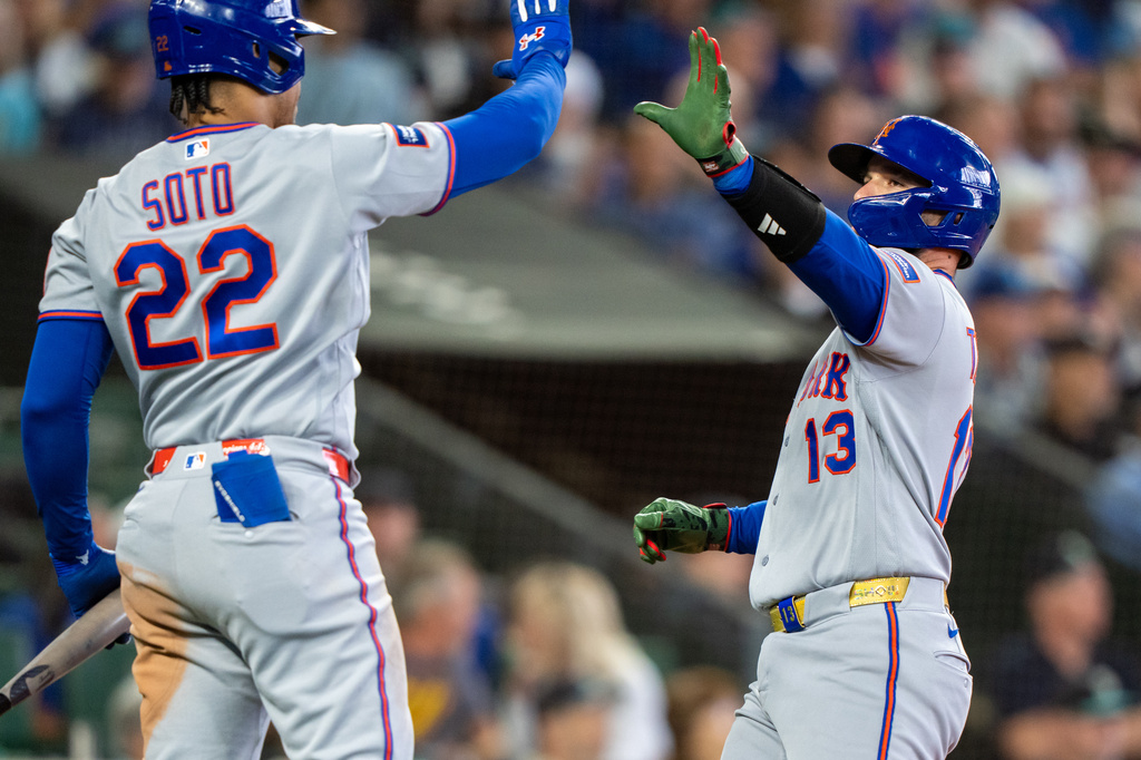 Two Mets players share a high-five on the field, Soto wearing #22 and a teammate #13 nearby against a blurred crowd backdrop.