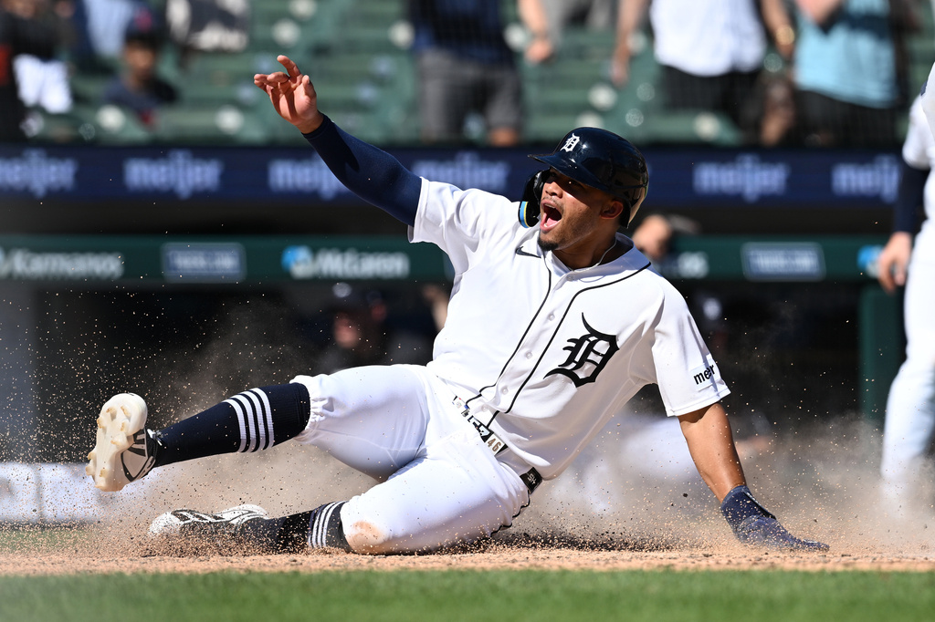 Detroit Tigers player sliding into a base, kicking up dirt with his arm raised.