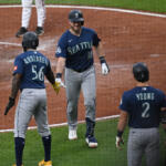 Three Seattle Mariners players in navy uniforms celebrate with a high-five on the infield dirt.