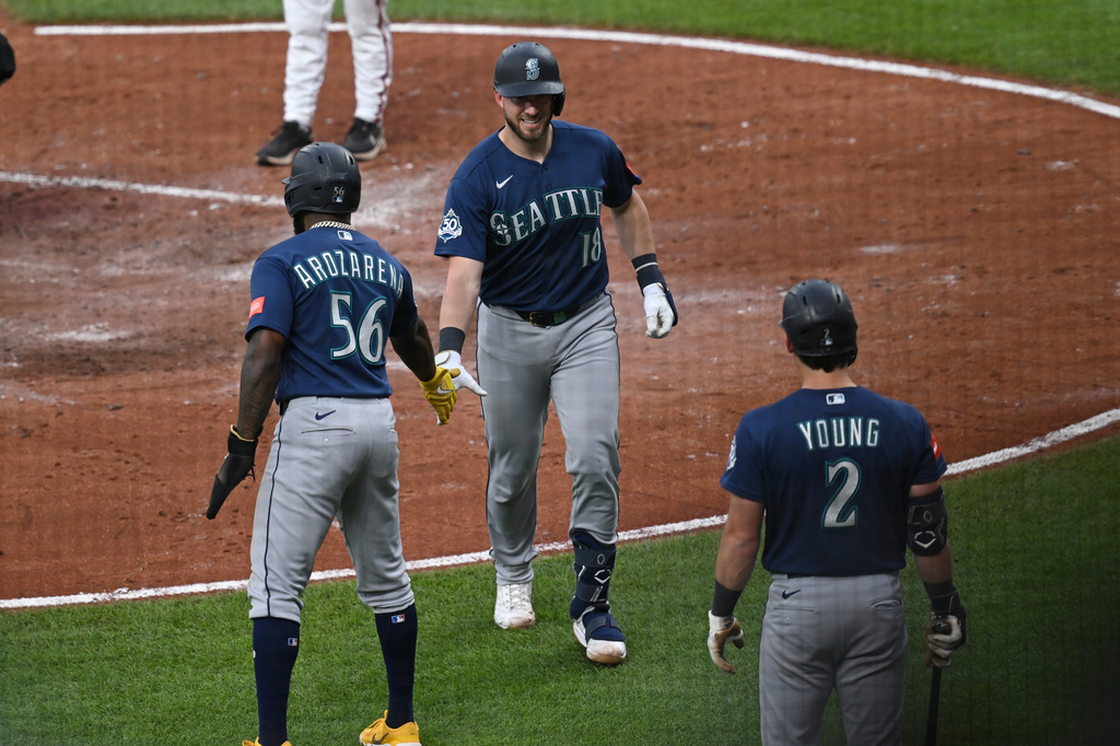 Three Seattle Mariners players in navy uniforms celebrate with a high-five on the infield dirt.