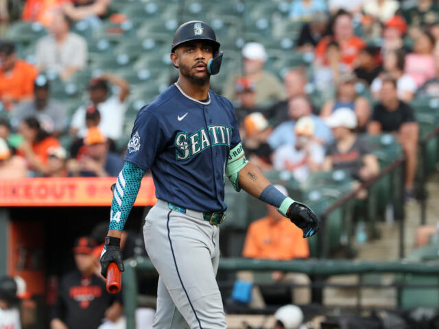 Seattle Mariners batter in navy uniform and helmet walking on the field during a game, crowd in the stands behind him.