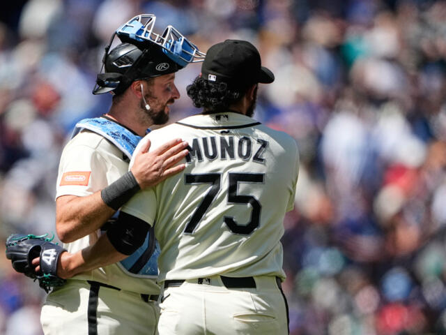 Two baseball players embrace on the field; back of Munoz's jersey shows number 75 as the crowd blurs in the background.