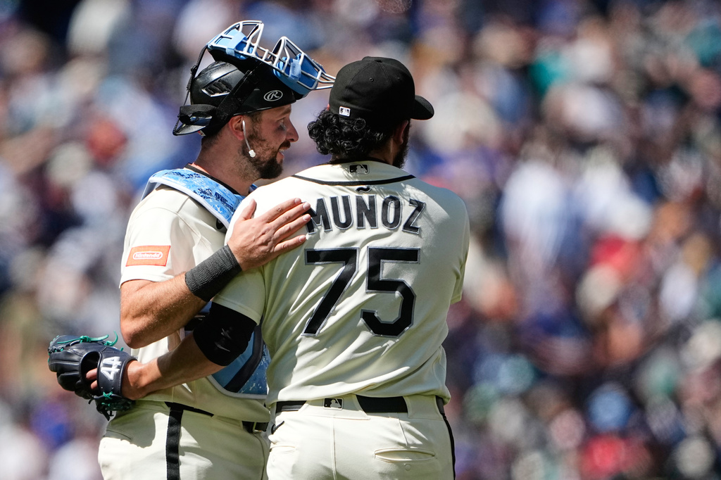 Two baseball players embrace on the field; back of Munoz's jersey shows number 75 as the crowd blurs in the background.
