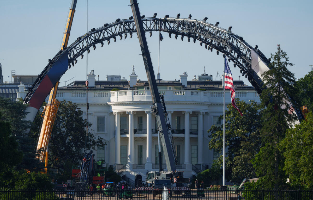 Large steel arch structure under construction in front of the White House, with a US flag nearby and workers on site.