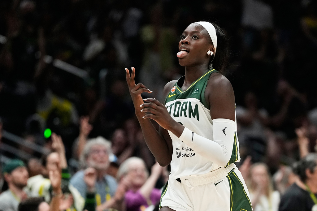 Female basketball player in a white and green Storm jersey on the court, sticking out her tongue as she moves.