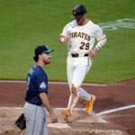 Pittsburgh Pirates player in white uniform #29 runs near home plate as an opposing player in blue watches from the infield dirt and grass nearby.