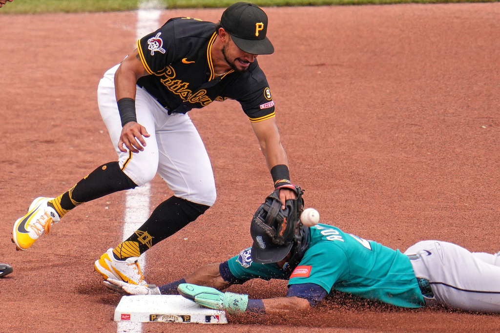 Pirates infielder in black and yellow stretches to tag a teal-uniformed runner sliding into a base; ball in midair near the glove at the base.