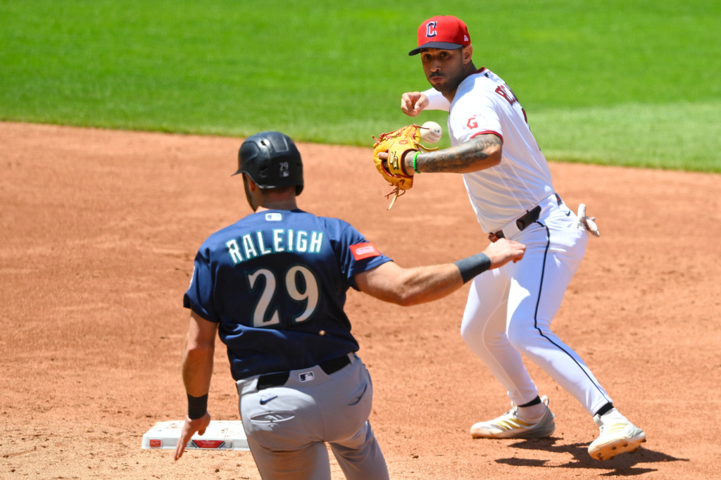 Baseball action: fielder in white throws as Raleigh 29 in blue watches near the base path on the dirt infield.