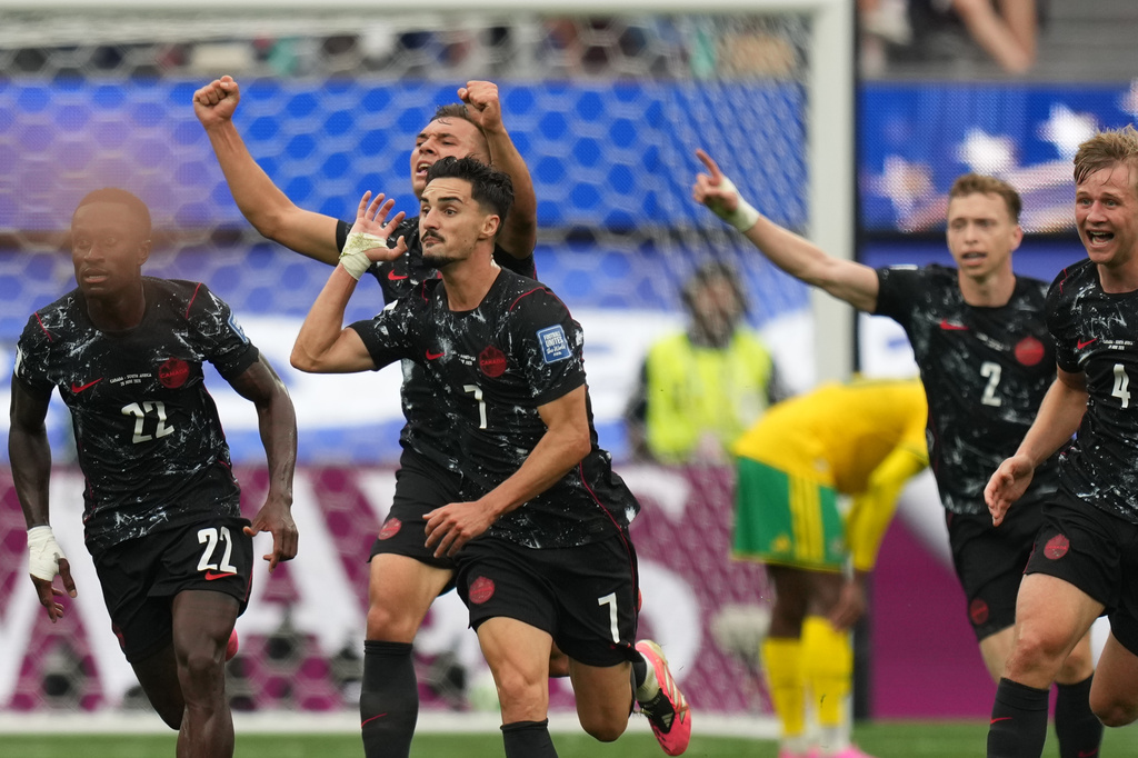 Soccer players in black uniforms celebrate a goal on the field, center player #1 signaling with a raised hand while teammates run with raised arms near the goal.