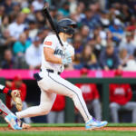 Baseball batter in a white uniform mid-swing as the crowd watches.