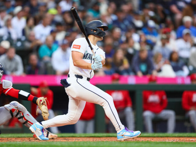 Baseball batter in a white uniform mid-swing as the crowd watches.