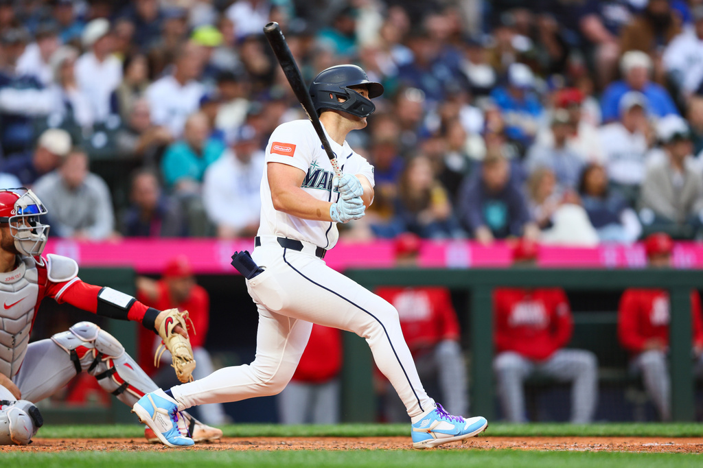 Baseball batter in a white uniform mid-swing as the crowd watches.