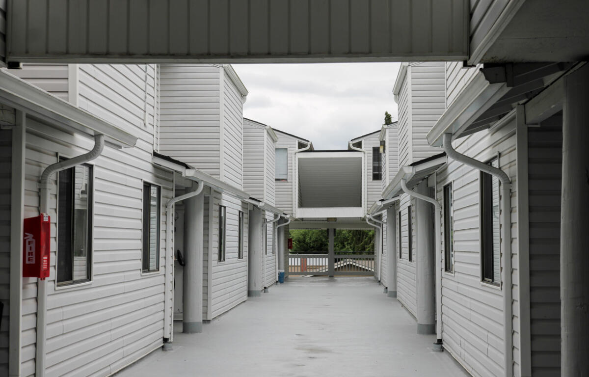 Open corridor between two white apartment buildings with a central elevated walkway and a red fire extinguisher mounted on the left wall.