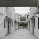 Open corridor between two white apartment buildings with a central elevated walkway and a red fire extinguisher mounted on the left wall.