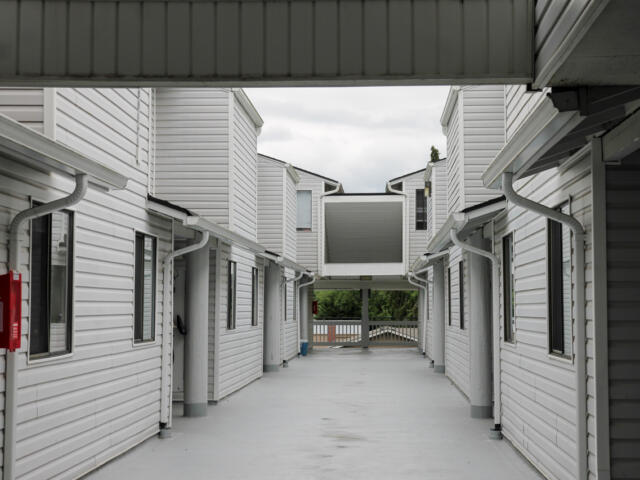 Open corridor between two white apartment buildings with a central elevated walkway and a red fire extinguisher mounted on the left wall.