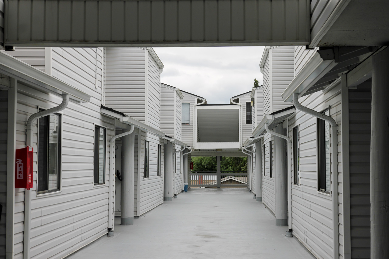 Open corridor between two white apartment buildings with a central elevated walkway and a red fire extinguisher mounted on the left wall.