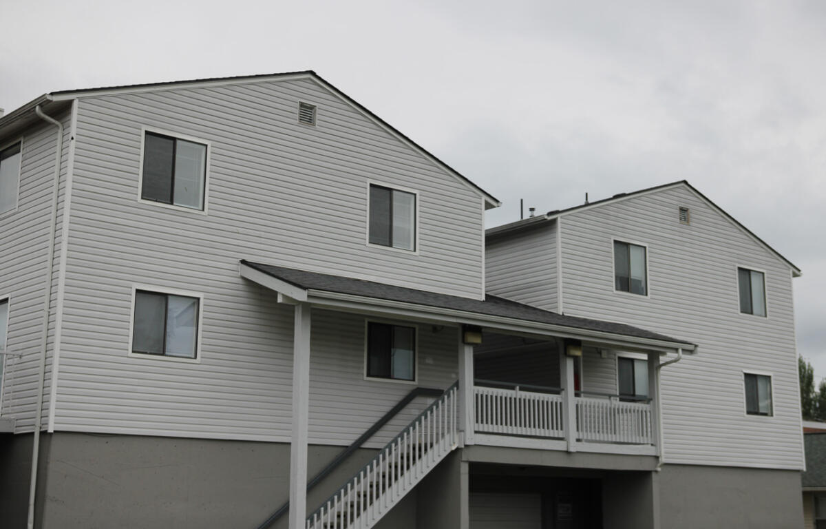 Two-story white siding apartment building with a covered porch and exterior stairs leading to the entryway.