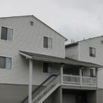 Two-story white siding apartment building with a covered porch and exterior stairs leading to the entryway.