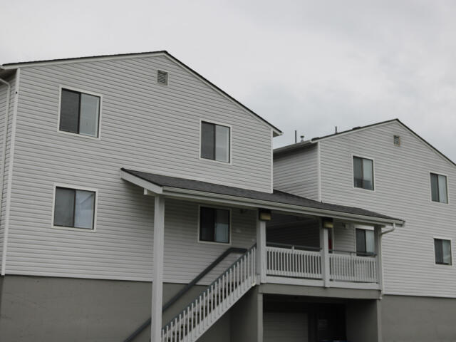 Two-story white siding apartment building with a covered porch and exterior stairs leading to the entryway.