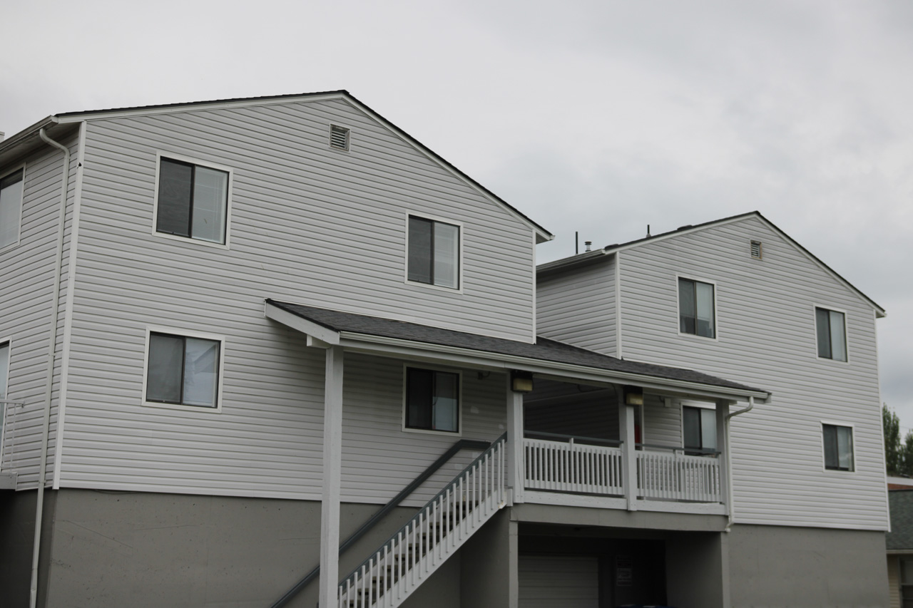 Two-story white siding apartment building with a covered porch and exterior stairs leading to the entryway.