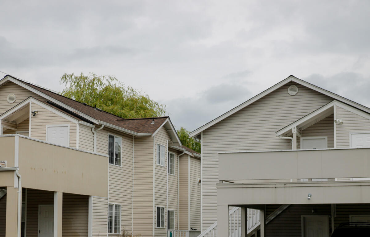 Row of beige two-story townhouses with white trim and balconies under a cloudy sky.