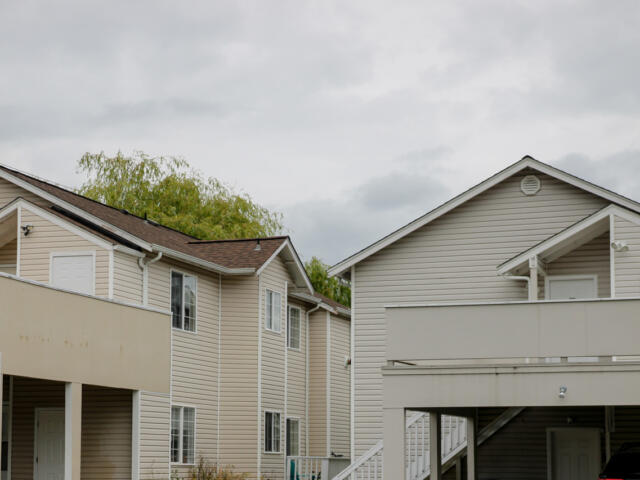 Row of beige two-story townhouses with white trim and balconies under a cloudy sky.