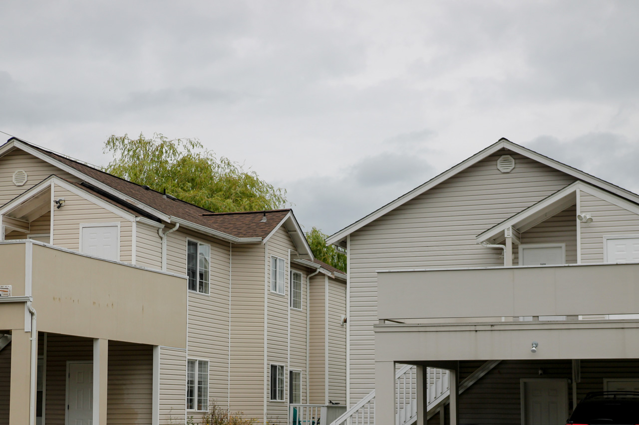 Row of beige two-story townhouses with white trim and balconies under a cloudy sky.