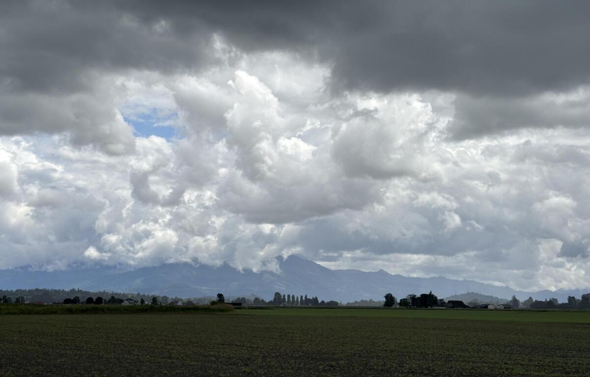 Flat farmland under dark storm clouds with a distant mountain range on the horizon.