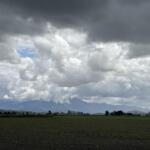 Flat farmland under dark storm clouds with a distant mountain range on the horizon.