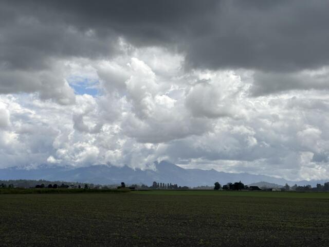 Flat farmland under dark storm clouds with a distant mountain range on the horizon.