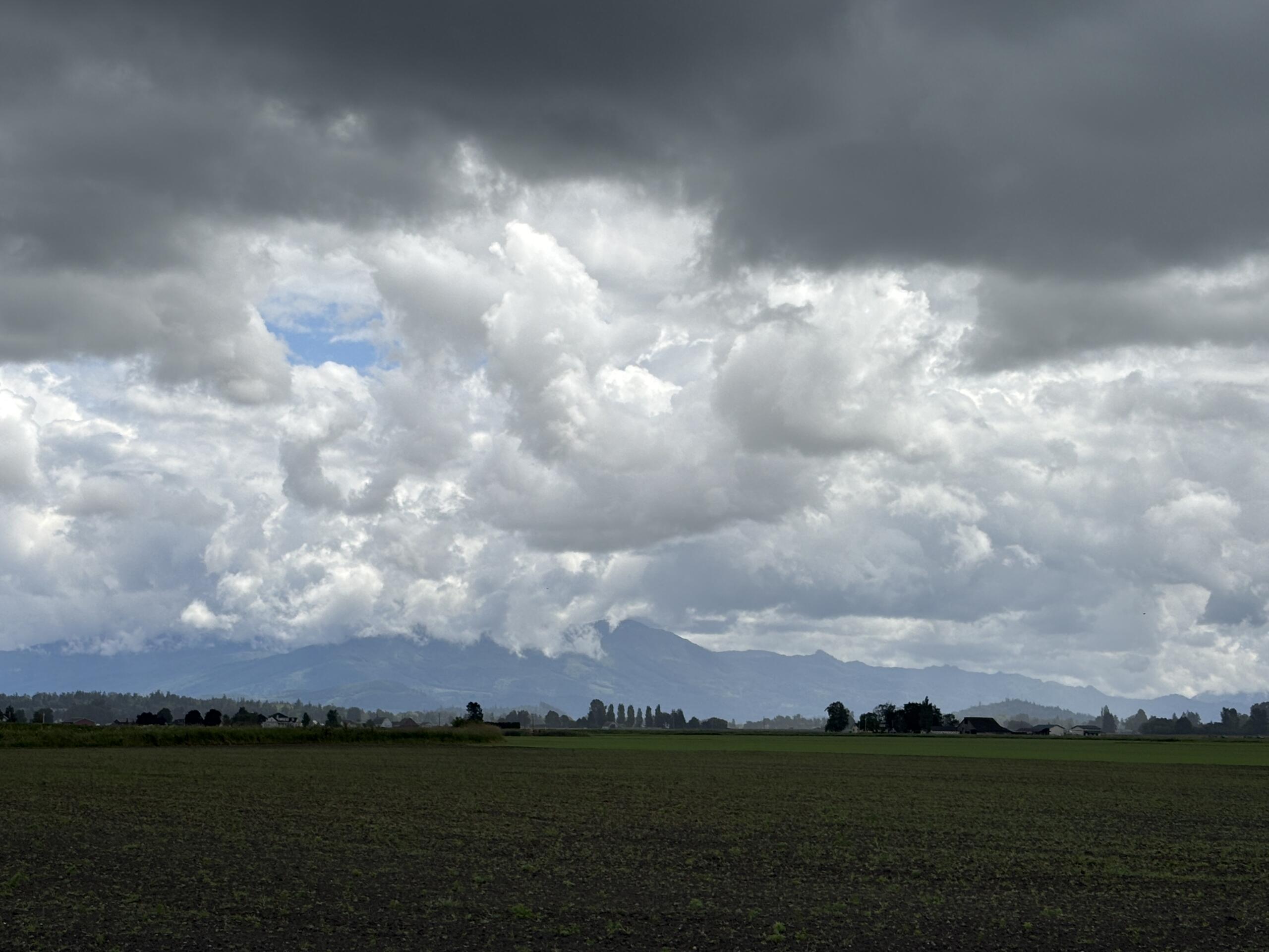 Flat farmland under dark storm clouds with a distant mountain range on the horizon.