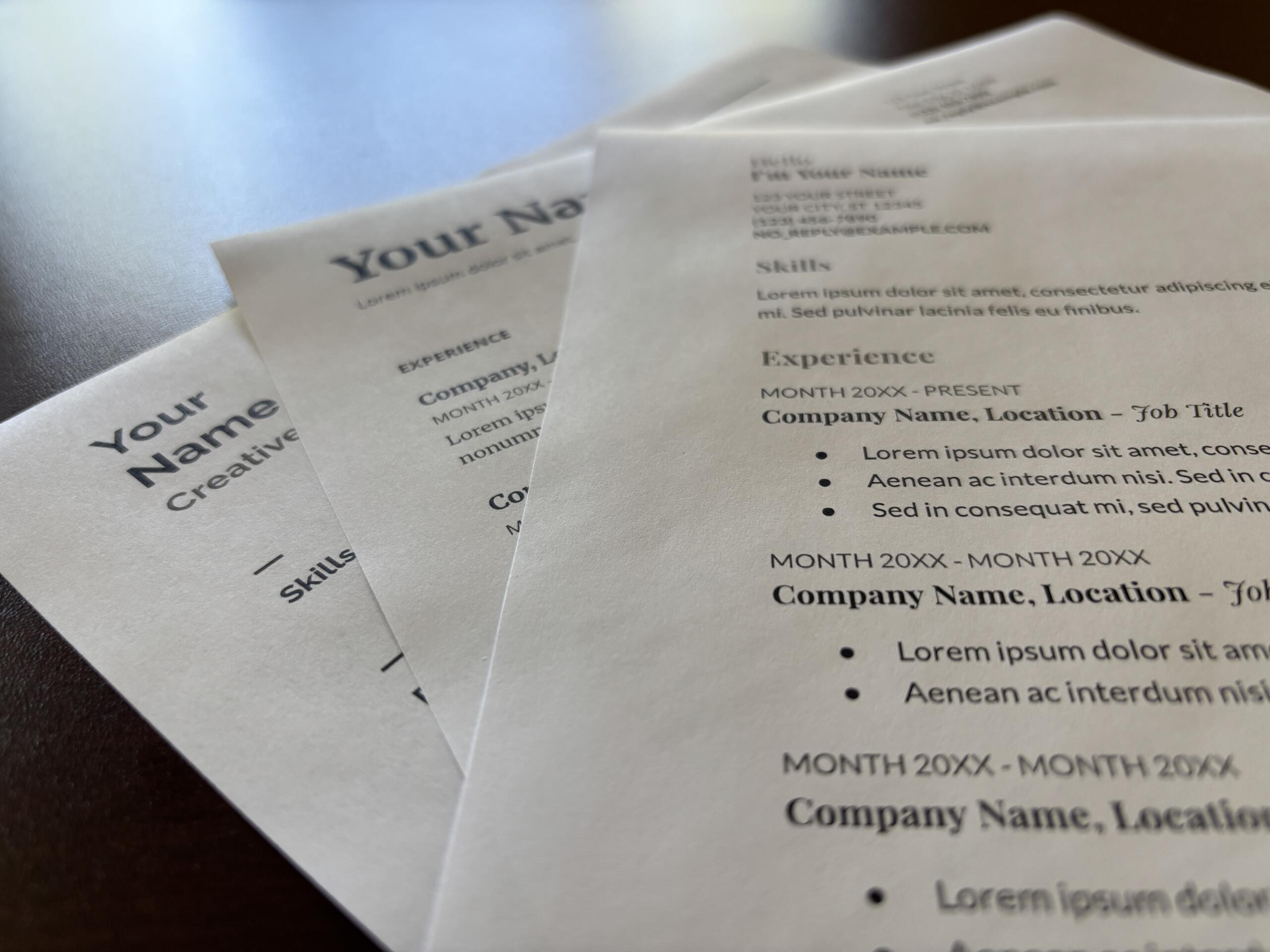 Close-up of printed resumes with placeholder text like 'Your Name', showing sections such as Experience and Skills on white paper.