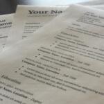 Close-up of overlapping resumes on a desk, showing placeholders like 'Your Name' and headings such as Experience and Skills with lorem ipsum text.