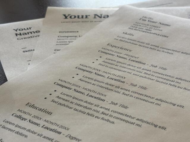 Close-up of overlapping resumes on a desk, showing placeholders like 'Your Name' and headings such as Experience and Skills with lorem ipsum text.