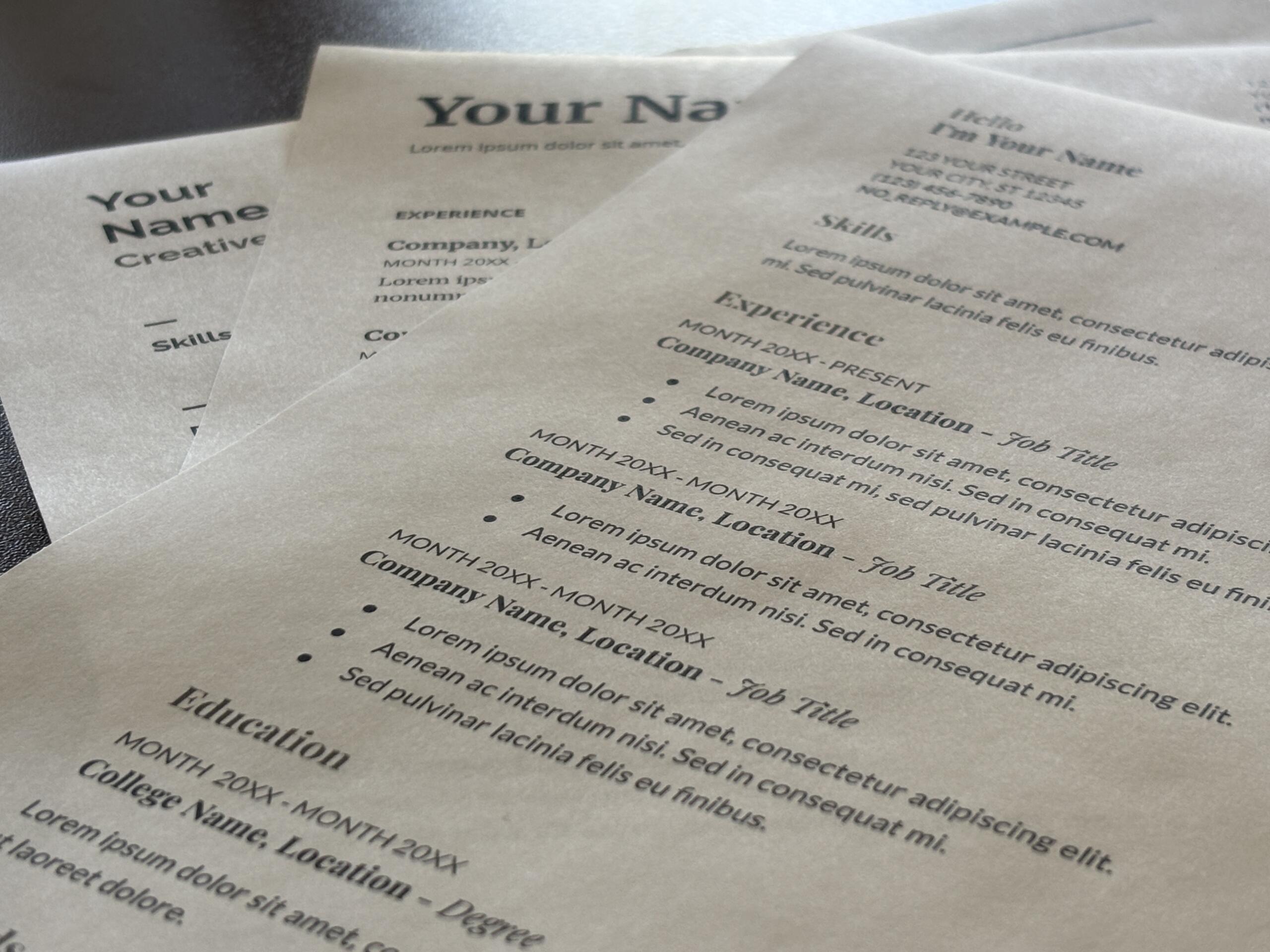 Close-up of overlapping resumes on a desk, showing placeholders like 'Your Name' and headings such as Experience and Skills with lorem ipsum text.