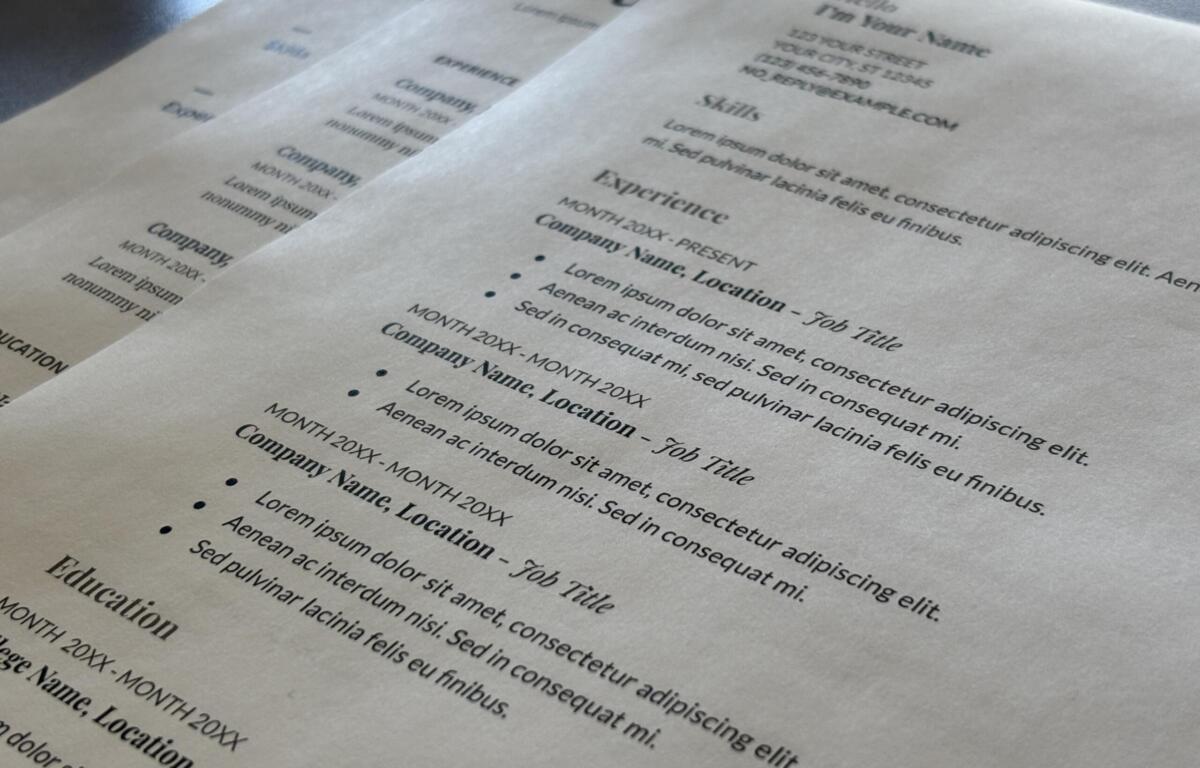 Multiple sheets of resume-style documents overlapped on a desk, with headings like Skills and Experience in lorem ipsum text (informational).