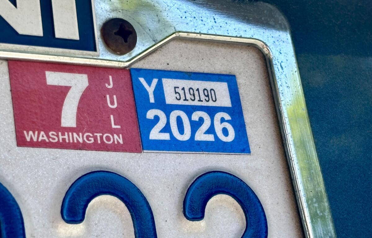 Close-up of a car's license plate area showing a red Washington state tab and a blue 2026 registration sticker near a screw.