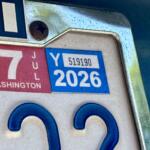 Close-up of a car's license plate area showing a red Washington state tab and a blue 2026 registration sticker near a screw.