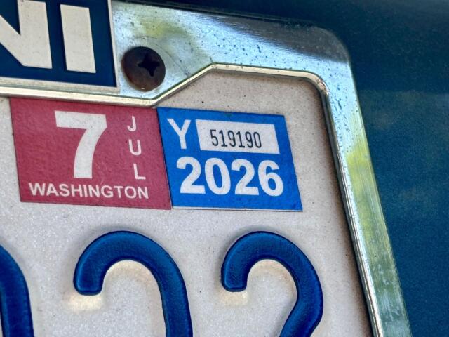 Close-up of a car's license plate area showing a red Washington state tab and a blue 2026 registration sticker near a screw.