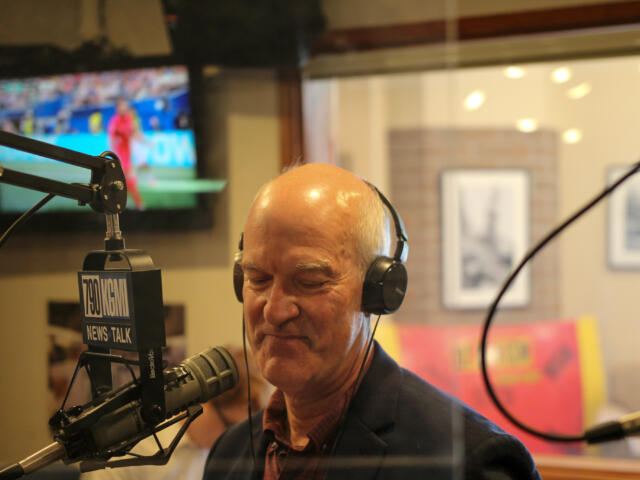 Man in a headset speaks into a professional mic in a radio studio with a 700 WLW News Talk sign visible in the foreground