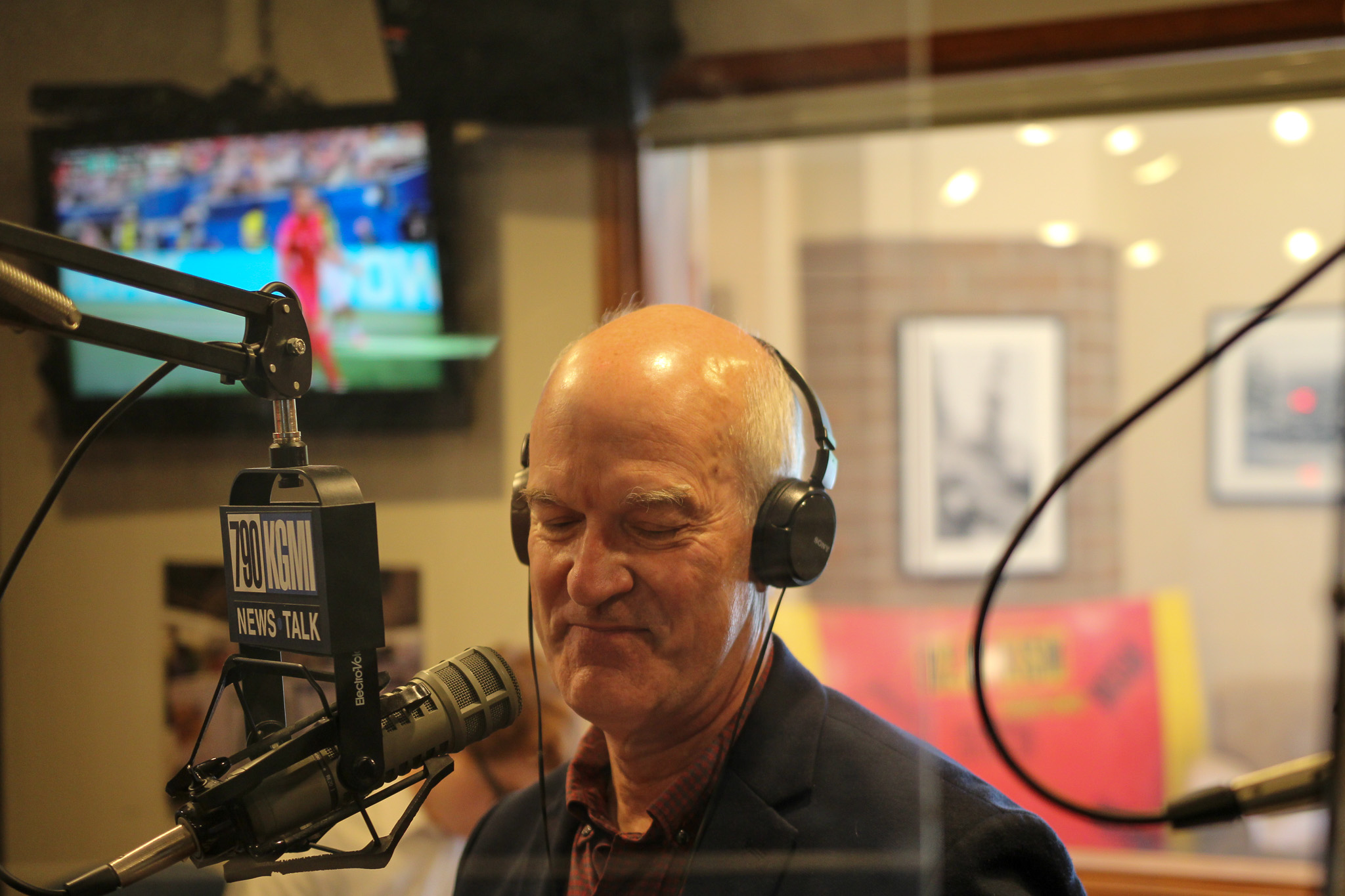 Man in a headset speaks into a professional mic in a radio studio with a 700 WLW News Talk sign visible in the foreground