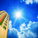 Thermometer in the lower-left foreground with a clear, radiant sun and blue sky, suggesting very hot weather (around 40–50°C).